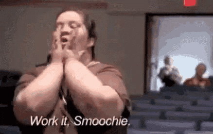a man is sitting in a auditorium with his hands on his face and says `` work it , smoochie '' .