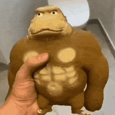 a person is holding a toy gorilla with muscles in their hand .