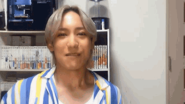 a man wearing a blue and yellow striped shirt is smiling in front of a bookshelf .