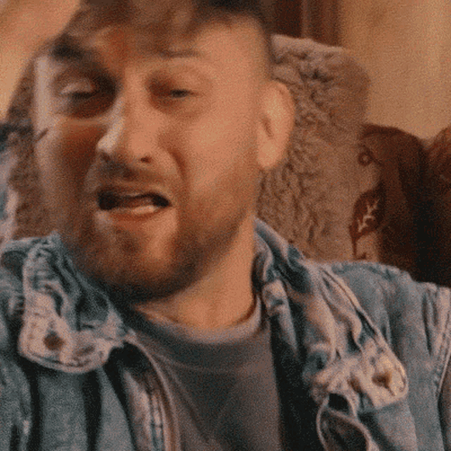 a man with a beard is sitting in a chair with his hand on his head and his mouth open