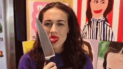 a woman is sticking her tongue out while holding a large knife in front of her face .