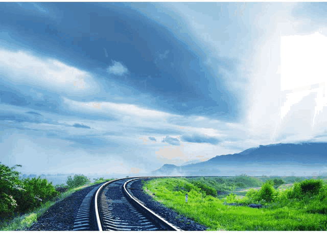 a train track with mountains in the background and a cloudy sky