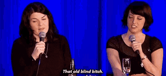 two women are talking into microphones on a stage and one of them is saying `` that old blind bitch . ''