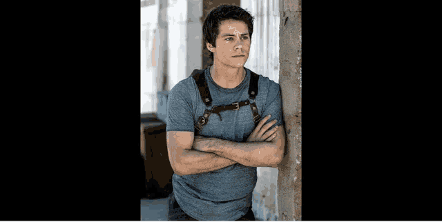 a young man with his arms crossed leaning against a wall .