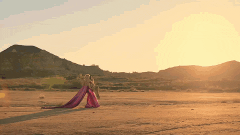 a woman in a pink dress is walking through a desert