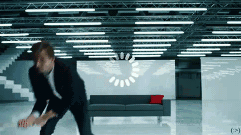 a man in a suit stands in a room with a loading circle in the background