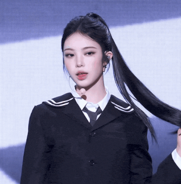 a woman in a black suit and tie is holding her hair in a ponytail