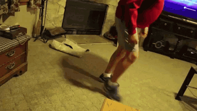 a man in a red sweatshirt is jumping in front of a tv that says playstation on it