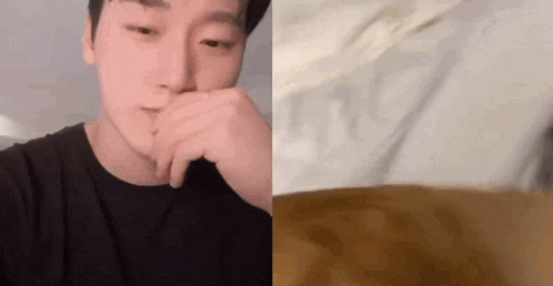 a man is covering his mouth with his hand and a cat is laying on a bed next to him .