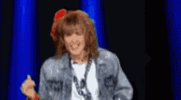a woman wearing a denim jacket and a red bow in her hair is dancing on a stage