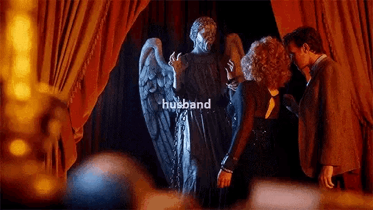 a man and a woman are standing next to a statue of an angel in a room .