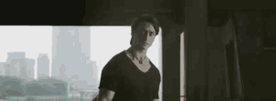 a man in a black shirt is standing in front of a window with a city in the background .