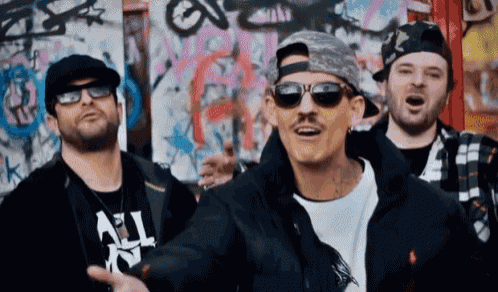 a group of men wearing sunglasses and hats are standing in front of a wall with graffiti on it that says all