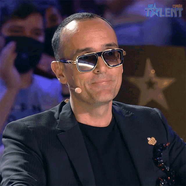 a man wearing sunglasses and a black suit is smiling in front of a sign that says " talent "