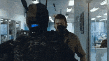 a man is standing next to a robot in a hallway holding a gun .