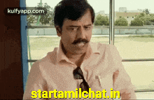 a man with a mustache is sitting in front of a window with the words starttamilchat.in in yellow letters