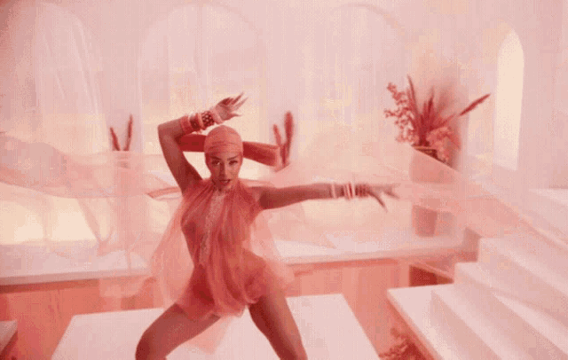 a woman in a pink dress is dancing in front of flowers