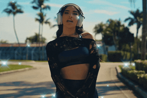 a woman wearing headphones and a crop top stands in front of palm trees