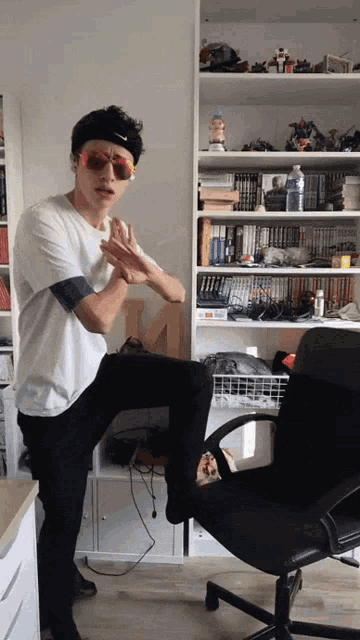 a man wearing sunglasses and a nike headband stands in front of a bookshelf