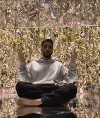 a man is sitting in a lotus position with his feet crossed in front of a wall of flowers .