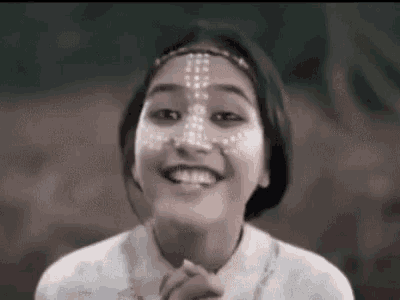 a woman with white paint on her face is smiling and praying .