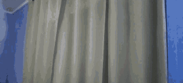 a man in a white shirt is standing in front of a curtain and holding his head .