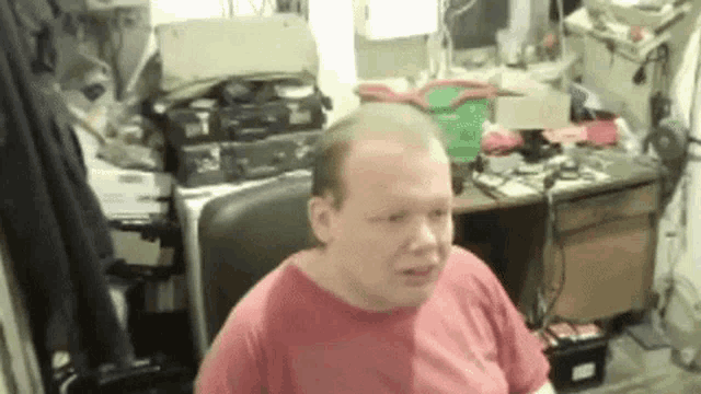a man in a red shirt is sitting in front of a desk .