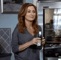 a woman is holding a bottle of beer in front of a fridge .