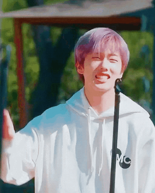 a young man with purple hair is singing into a microphone while wearing a white hoodie that says mc on it