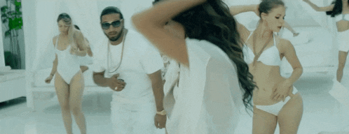a group of women in bikinis are dancing with a man wearing sunglasses