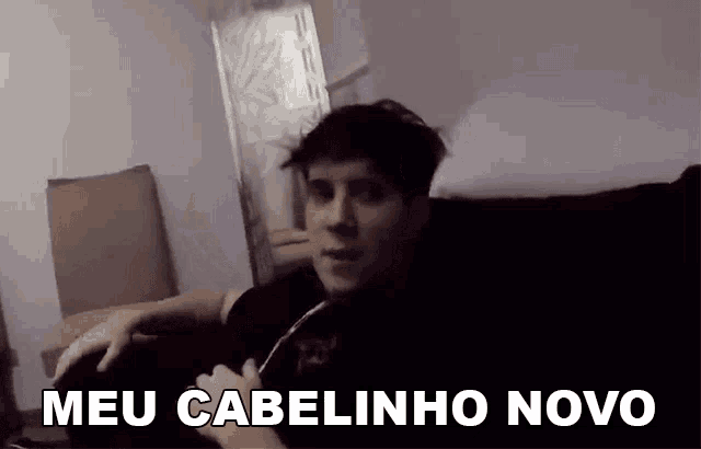 a man is sitting on a couch with the words meu cabelinho novo written above him