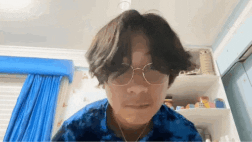 a young man wearing glasses and a tie dye shirt is sitting in a room .