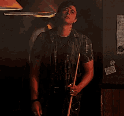a man is holding a pool cue in his hand in a dark room .