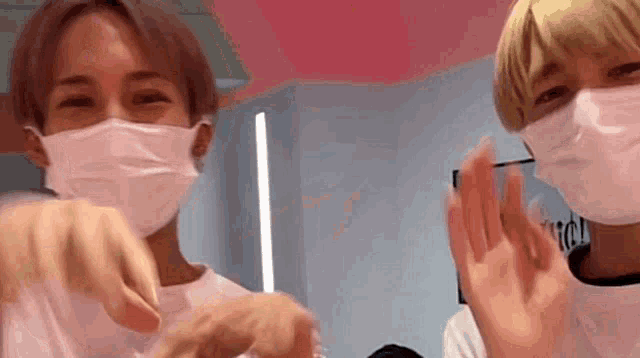 two young men wearing face masks are standing next to each other and making funny faces .
