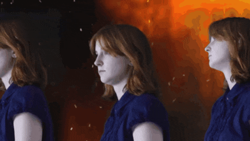 a woman in a blue shirt is standing in front of a fire background