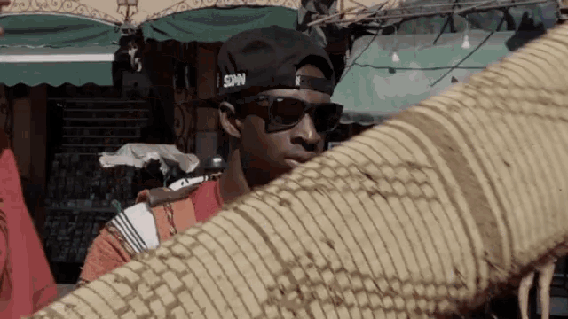 a man wearing sunglasses and a sdn hat holds a piece of fabric
