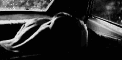 a black and white photo of a person sitting in a car looking out the window .