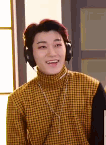 a young man wearing headphones and a plaid shirt is smiling and looking at the camera .