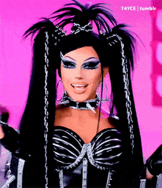 a drag queen with long black hair and a choker is smiling and wearing a black and silver outfit .