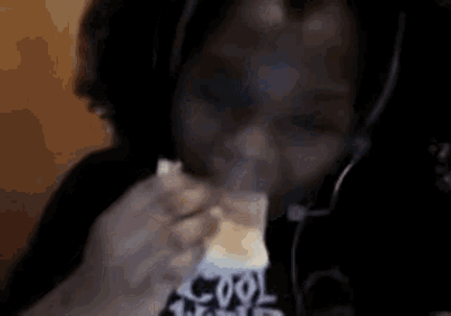 a young boy wearing headphones is eating a sandwich while looking at the camera .