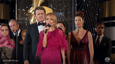 a woman in a pink dress is singing into a microphone while standing in front of a group of people .