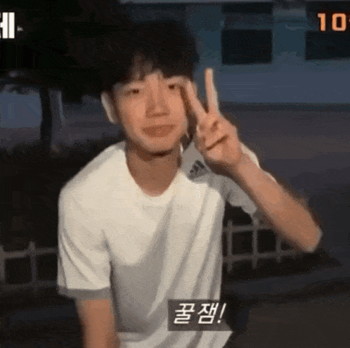 a young man in a white shirt is giving a peace sign