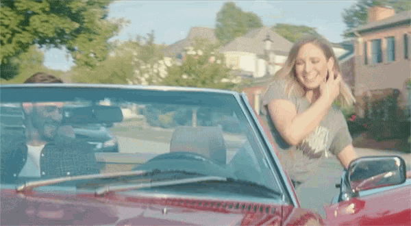 a woman is sitting in a red convertible car talking on a cell phone .
