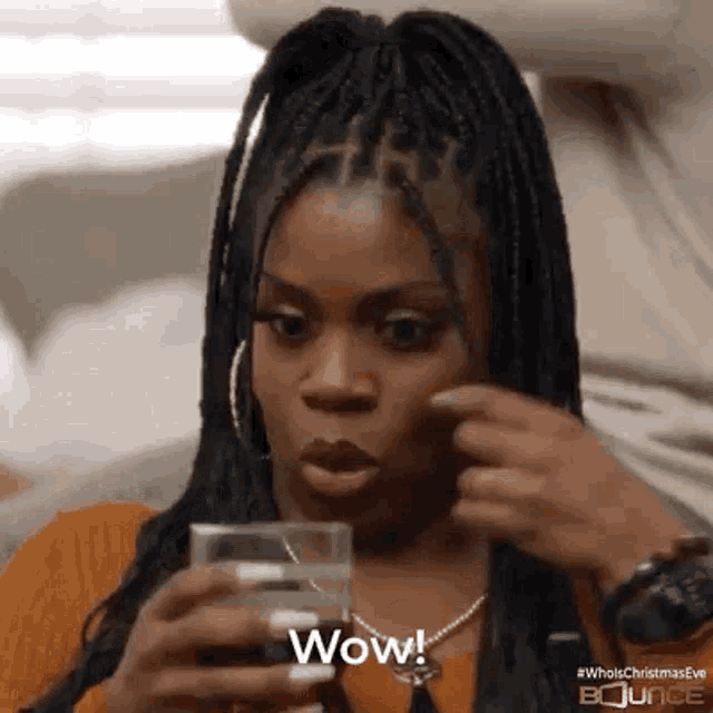 a woman with braids is holding a glass of water and making a funny face .