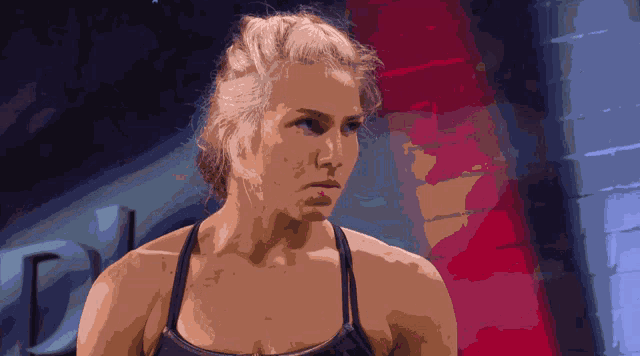 a woman in a black tank top stands in front of a brick wall