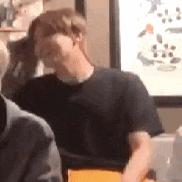 a man in a black shirt is sitting at a table with his head in his hand .