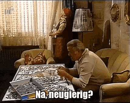 a man is sitting at a table with a box of puzzles and the words na neugierig written on the bottom