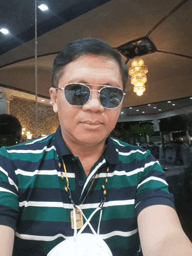 a man wearing sunglasses and a striped shirt has a lanyard around his neck that says ' a '