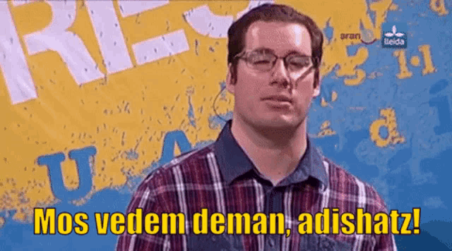 a man wearing glasses and a plaid shirt says " mos vedem deman adishatz "