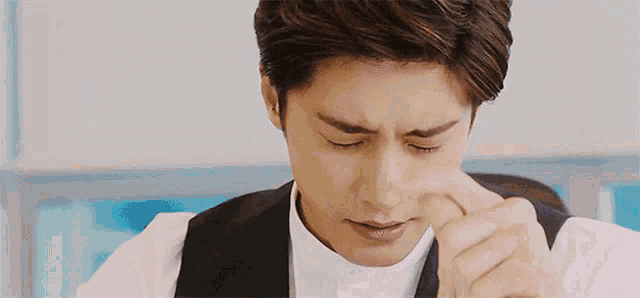 a man in a white shirt and black vest is rubbing his nose